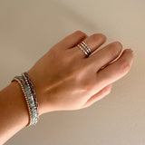 Hand wearing multiple rings and bracelets on a neutral background