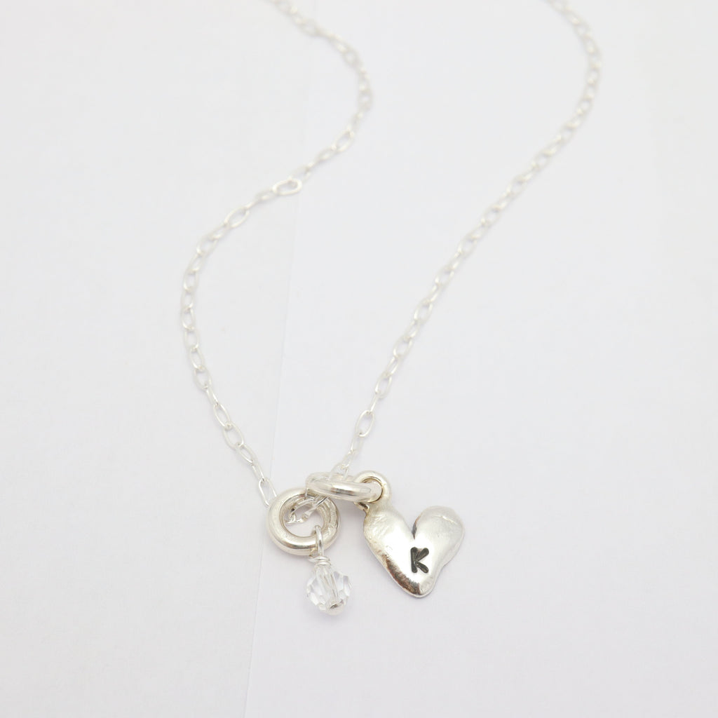 Silver initial-stamped heart necklace featuring a clear Austrian crystal
