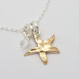 Gold starfish pendant on a silver chain with a clear crystal charm against a light gray background