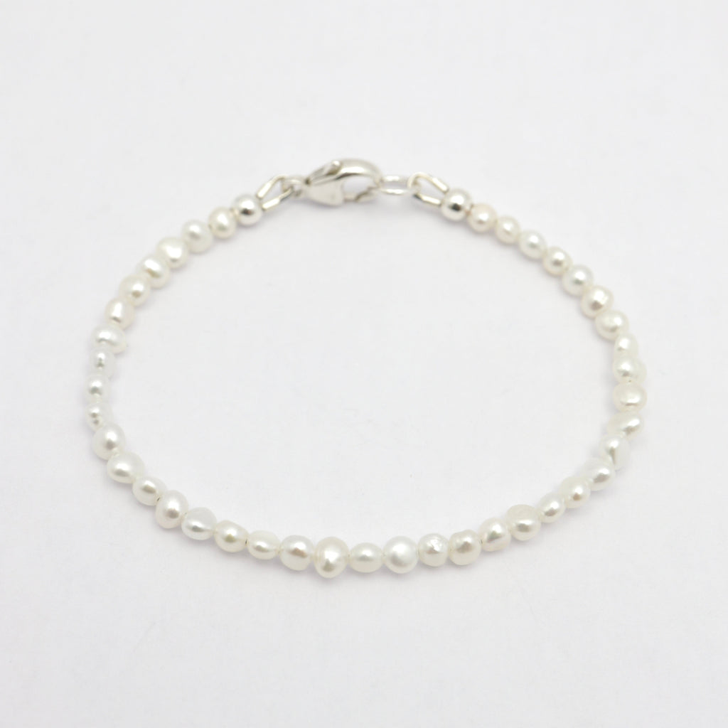 A delicate bracelet made of small white freshwater pearls linked with a polished silver clasp, displayed on a clean white background.