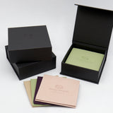 Black jewelry box with pouches in beige, sage, plum, and pink, all featuring the Orange Avocado Jewelry logo