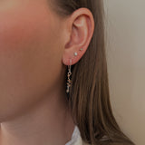 Close-up of a person wearing a delicate earring with a neutral background